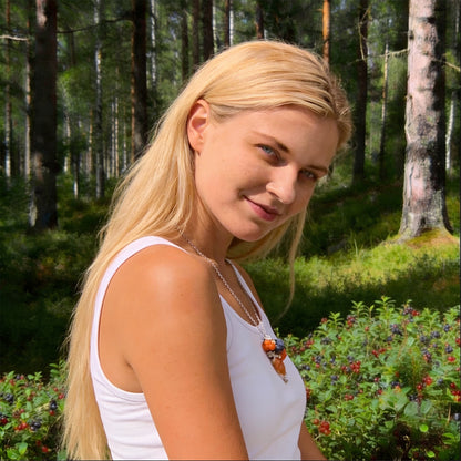 Blonde woman wearing the Berry Forest Necklace in a sunlit Nordic forest surrounded by berry bushes. Handmade necklace with hand-shaped berries and leaves, photographed in natural summer light. Handmade in Finland by byMinta.