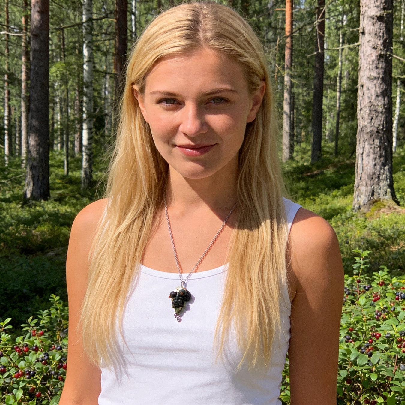 Scandinavian woman wearing a handmade berry necklace featuring blackcurrants, blackberries, green leaves, a white flower and purple crystal accents. Portrait photographed in a Nordic forest surrounded by berry shrubs in bright natural daylight.