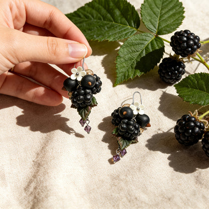 erry Harvest Earrings photographed with fresh berries and green leaves in soft natural light, with one earring gently held by hand for scale. Handmade in Finland by byMinta.