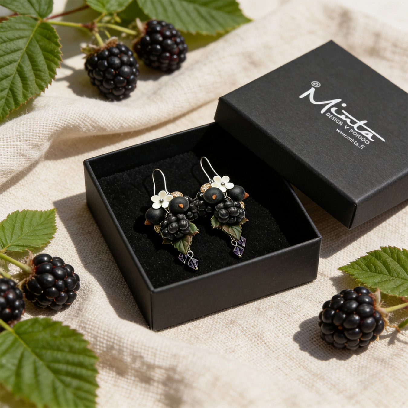Berry Harvest Earrings presented in a gift box, surrounded by natural linen fabric, fresh blackberries, and green leaves. Handmade in Finland by byMinta.