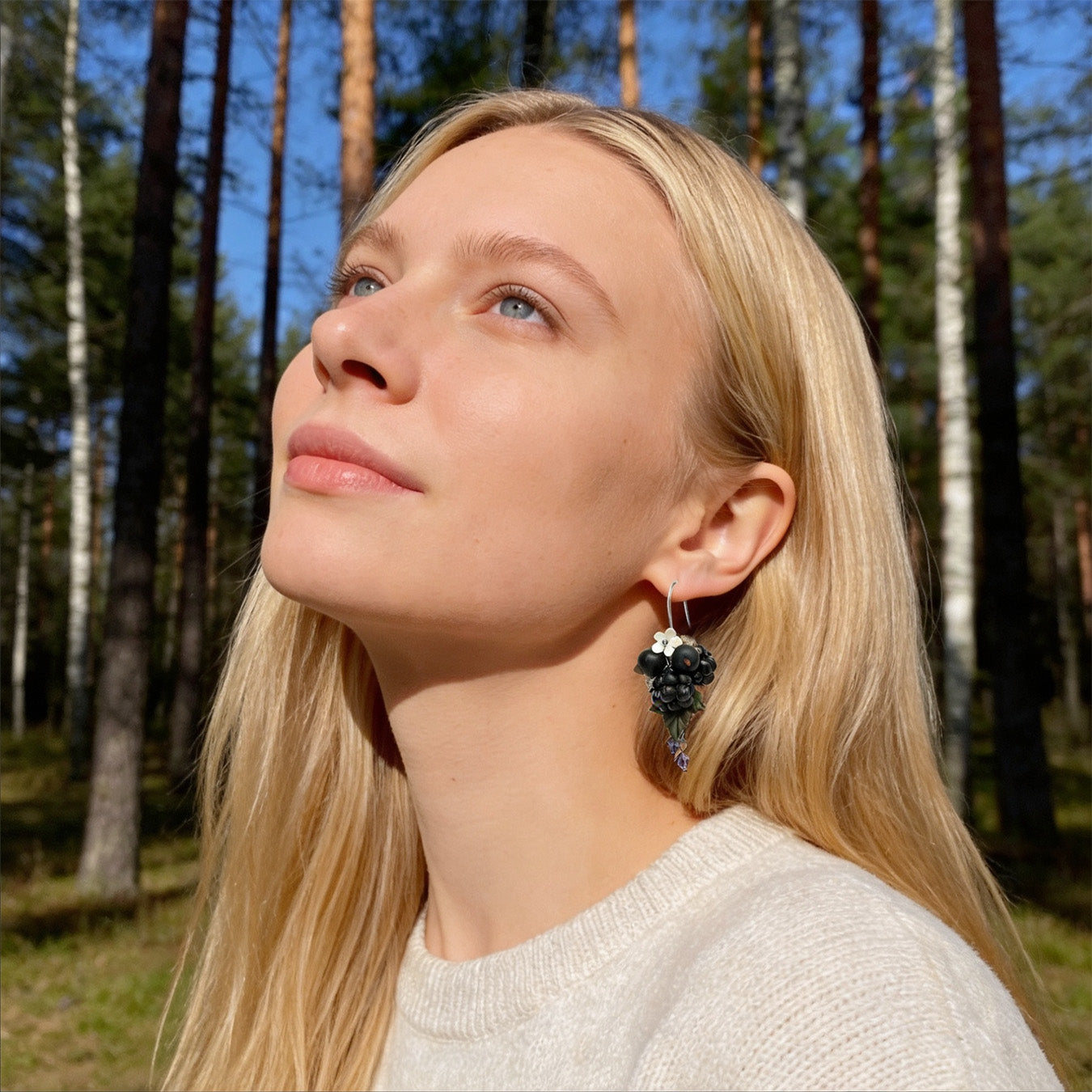 Blonde woman wearing Berry Harvest Earrings in a sunlit Nordic forest. Handmade earrings inspired by the rich colors of late-summer berries.