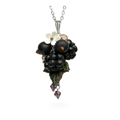 Handmade berry necklace featuring sculpted blackcurrants, blackberries, leaves and a small white flower. Detailed botanical statement jewelry on a fine chain against a clean white background, handcrafted in Finland.