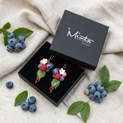 Dancing Berries Earrings presented in a gift box, surrounded by natural linen fabric, fresh raspberries, blueberries, and green leaves. Handmade in Finland by byMinta.