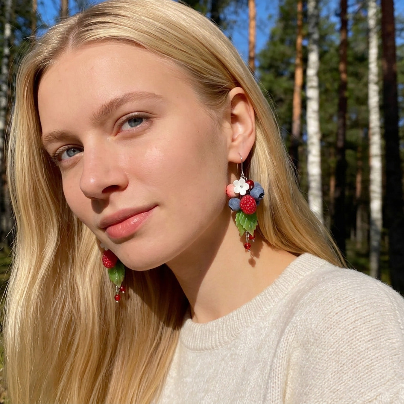 Blonde woman wearing Dancing Berries Earrings in a sunlit Nordic forest. Handmade earrings inspired by the joyful colors of summer berries.