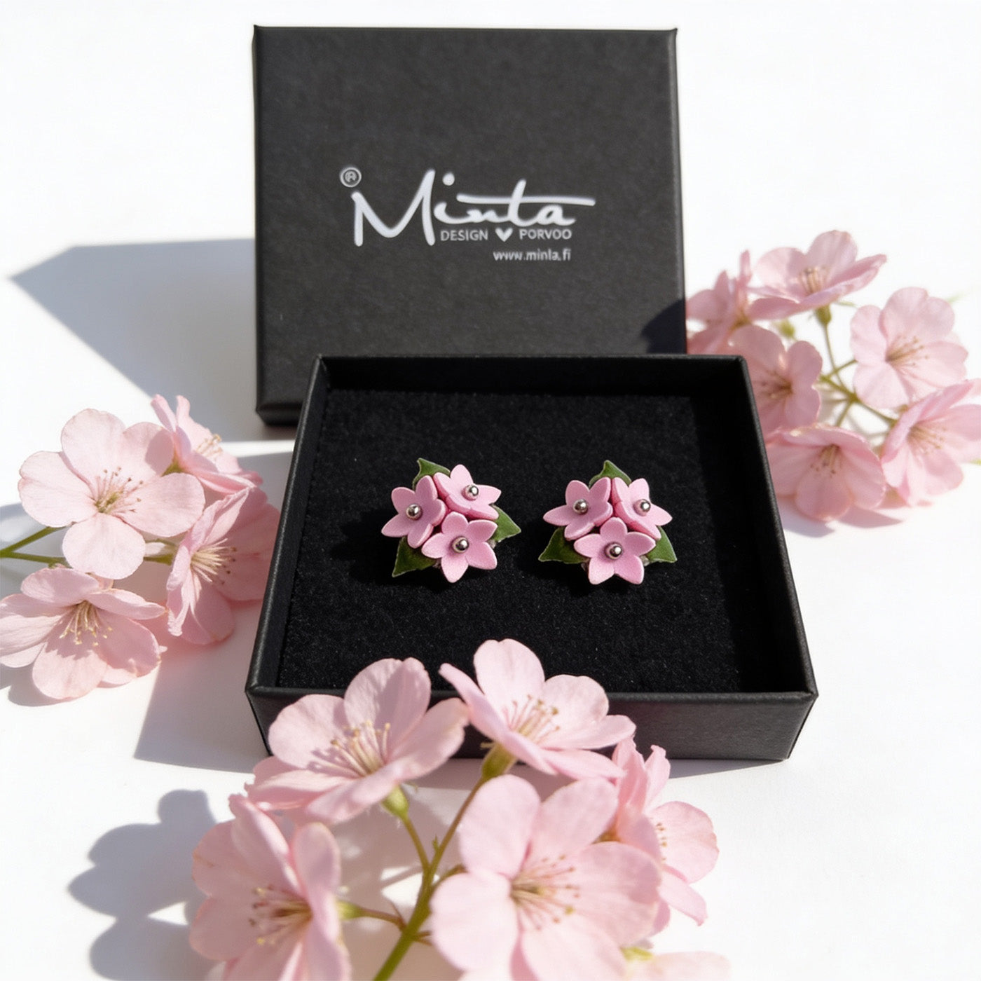 Pink Forest Star stud earrings in a black byMinta jewelry box surrounded by soft pink flowers, handmade in Finland and inspired by Nordic forest nature.