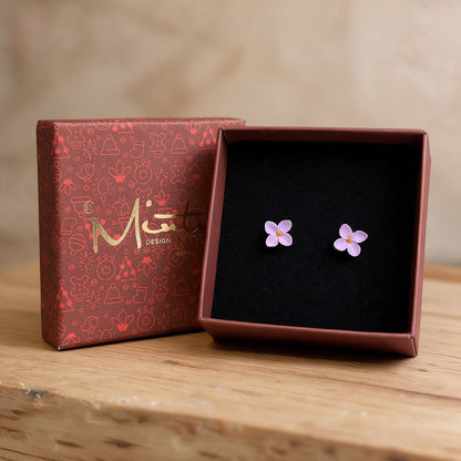 Lilac flower stud earrings made in Finland, displayed in a burgundy byMinta jewelry gift box with black velvet lining, photographed on a wooden surface.