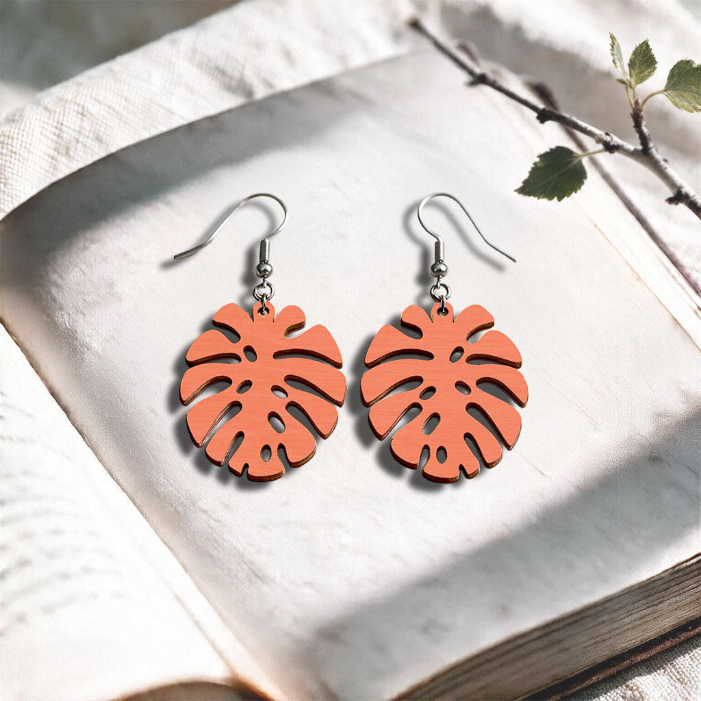 Coral Monstera plywood earrings handcrafted in Finland, photographed on a vintage book in natural sunlight