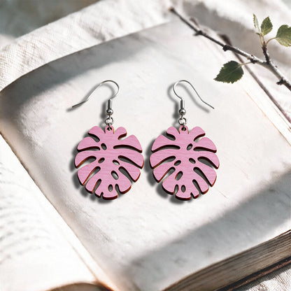 Mauve Monstera plywood earrings handcrafted in Finland, photographed on a vintage book in natural sunlight