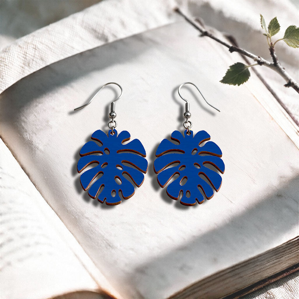 Blue Monstera plywood earrings handcrafted in Finland, photographed on a vintage book in natural sunlight