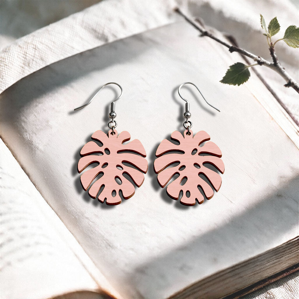 Light pink Monstera plywood earrings handcrafted in Finland, photographed on a vintage book in natural sunlight