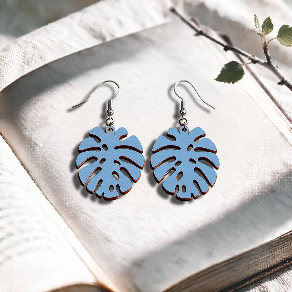 Light blue Monstera plywood earrings handcrafted in Finland, photographed on a vintage book in natural sunlight