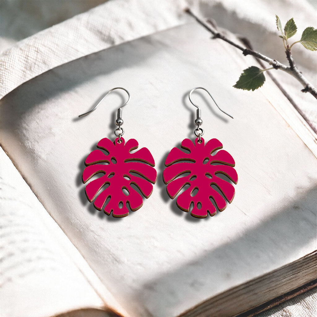 Raspberry Monstera plywood earrings handcrafted in Finland, photographed on a vintage book in natural sunlight