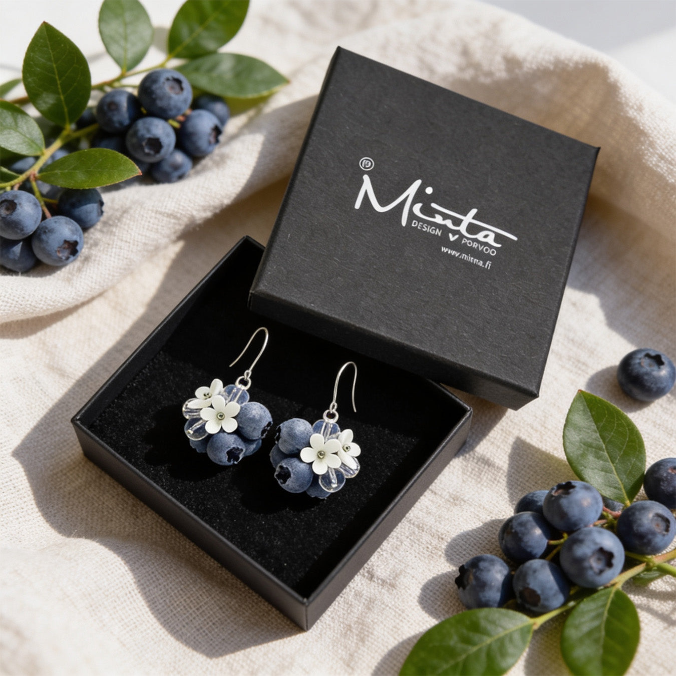 Blueberry Bouquet Earrings presented in a gift box, surrounded by natural linen fabric, fresh blueberries, and green leaves. Handmade in Finland by byMinta.