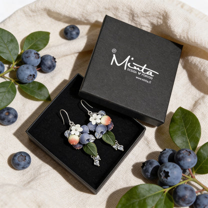 Blueberry Branch Earrings presented in a gift box, surrounded by natural linen fabric, fresh blueberries, and blueberry leaves. Handmade in Finland by byMinta.