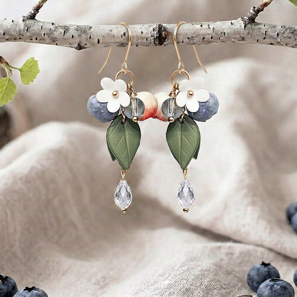 Berry earrings with blueberries, flowers, leaves and crystal drops, handmade in Finland, photographed on a birch branch in a Scandinavian setting
