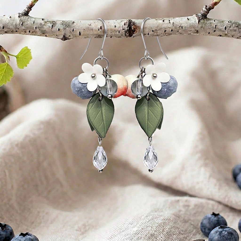 Berry earrings with blueberries, flowers, leaves and crystal drops, handmade in Finland, photographed on a birch branch in a Scandinavian setting