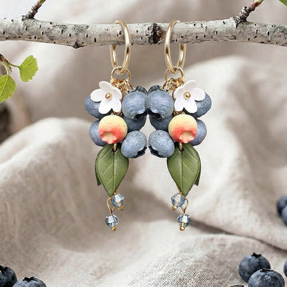 Berry Huggie hoop earrings with blueberries, flowers, leaves and crystal drops, handmade in Finland, photographed on a birch branch in a Scandinavian setting