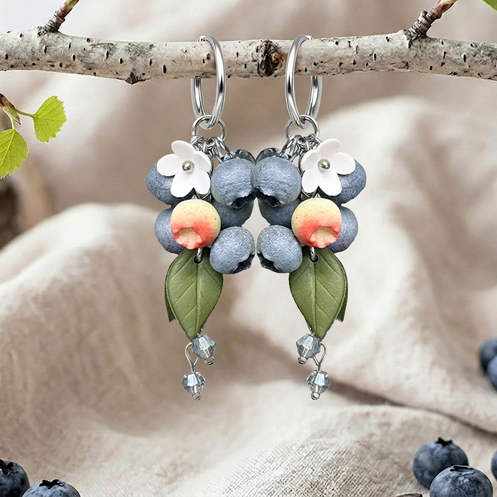 Berry Huggie hoop earrings with blueberries, flowers, leaves and crystal drops, handmade in Finland, photographed on a birch branch in a Scandinavian setting