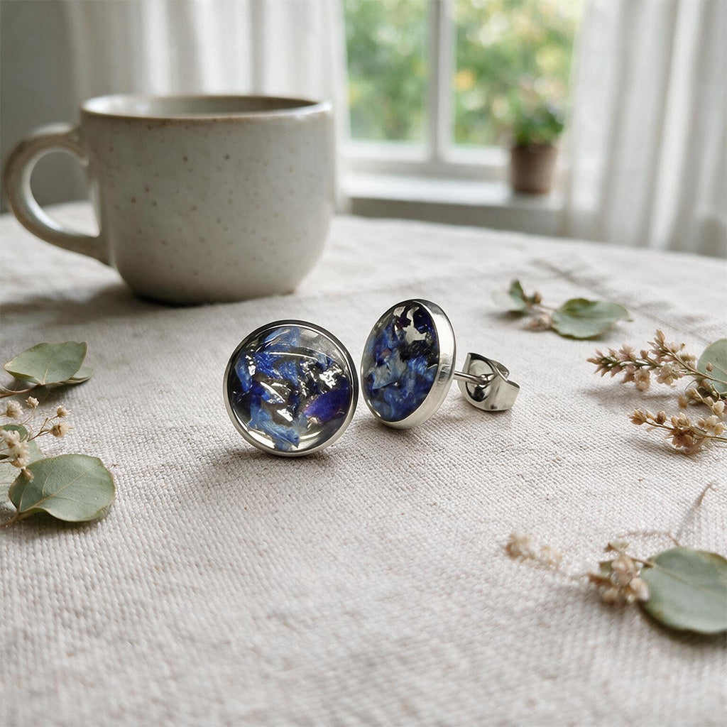 Handmade resin stud earrings with real blue hydrangea petals in stainless steel settings on natural linen.