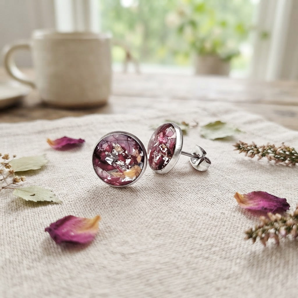 Handmade rose petal stud earrings with real preserved rose petals and silver leaf, displayed on natural linen with scattered petals in soft natural light.