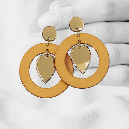 Lion Yellow  NiinMua plywood stud earrings with gold mirror acrylic teardrops, made in Finland, photographed against a black-and-white hand background.