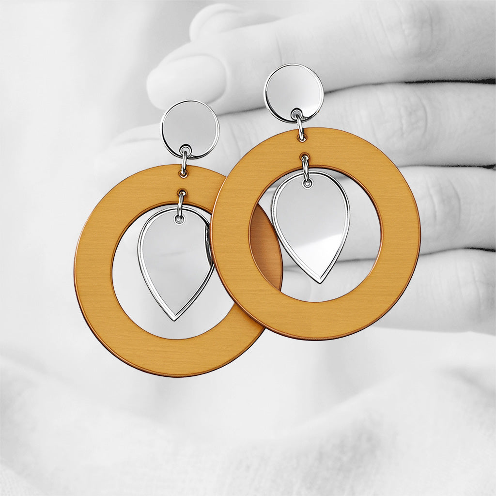 Lion yellow NiinMua plywood stud earrings with silver mirror acrylic teardrops, made in Finland, photographed against a black-and-white hand background.