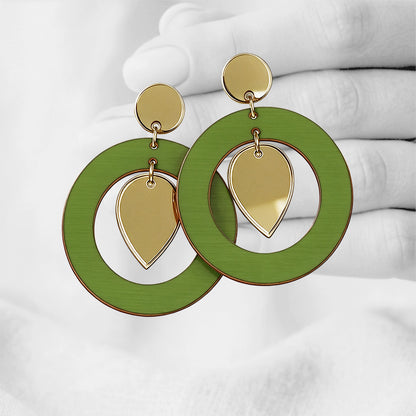 Green NiinMua plywood stud earrings with gold mirror acrylic teardrops, made in Finland, photographed against a black-and-white hand background.