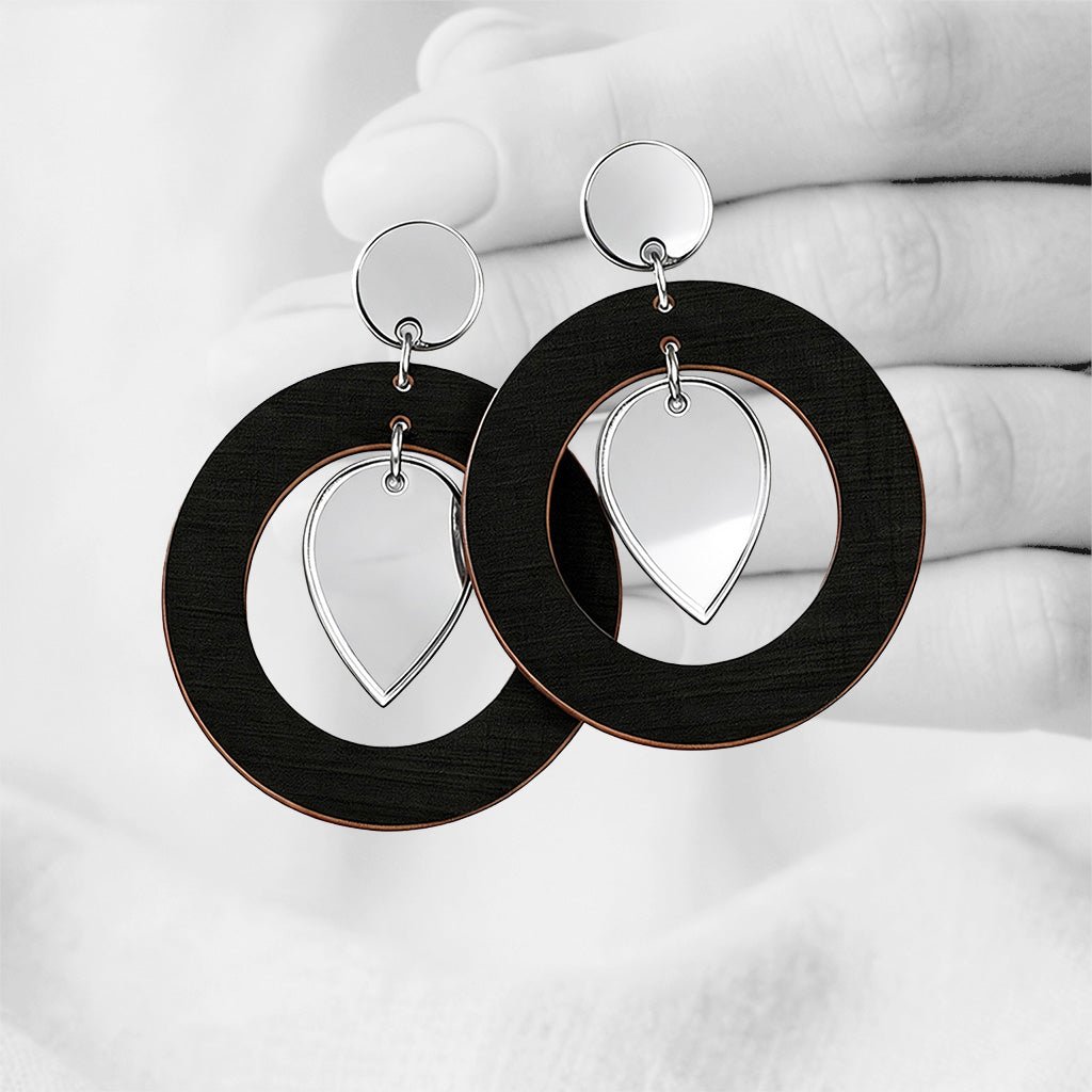 BlackNiinMua plywood stud earrings with silver mirror acrylic teardrops, made in Finland, photographed against a black-and-white hand background.