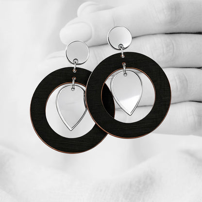 BlackNiinMua plywood stud earrings with silver mirror acrylic teardrops, made in Finland, photographed against a black-and-white hand background.