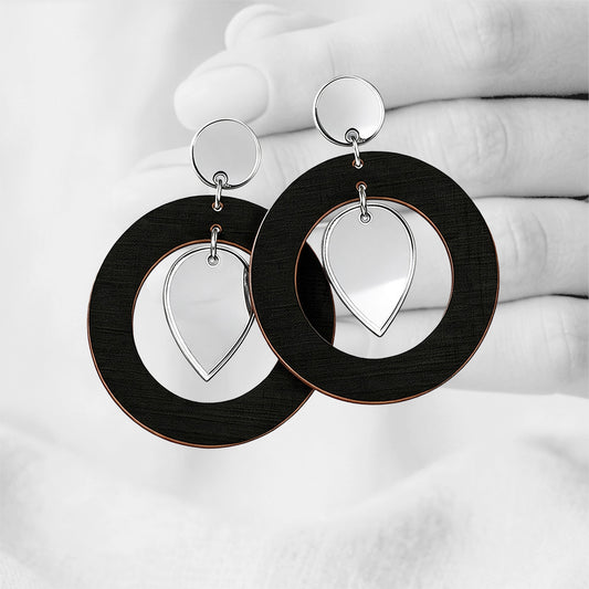 BlackNiinMua plywood stud earrings with silver mirror acrylic teardrops, made in Finland, photographed against a black-and-white hand background.
