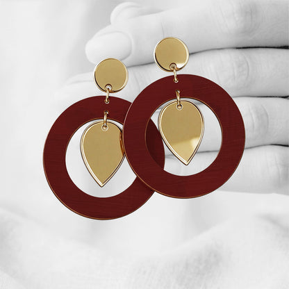 Rust NiinMua plywood stud earrings with gold mirror acrylic teardrops, made in Finland, photographed against a black-and-white hand background.