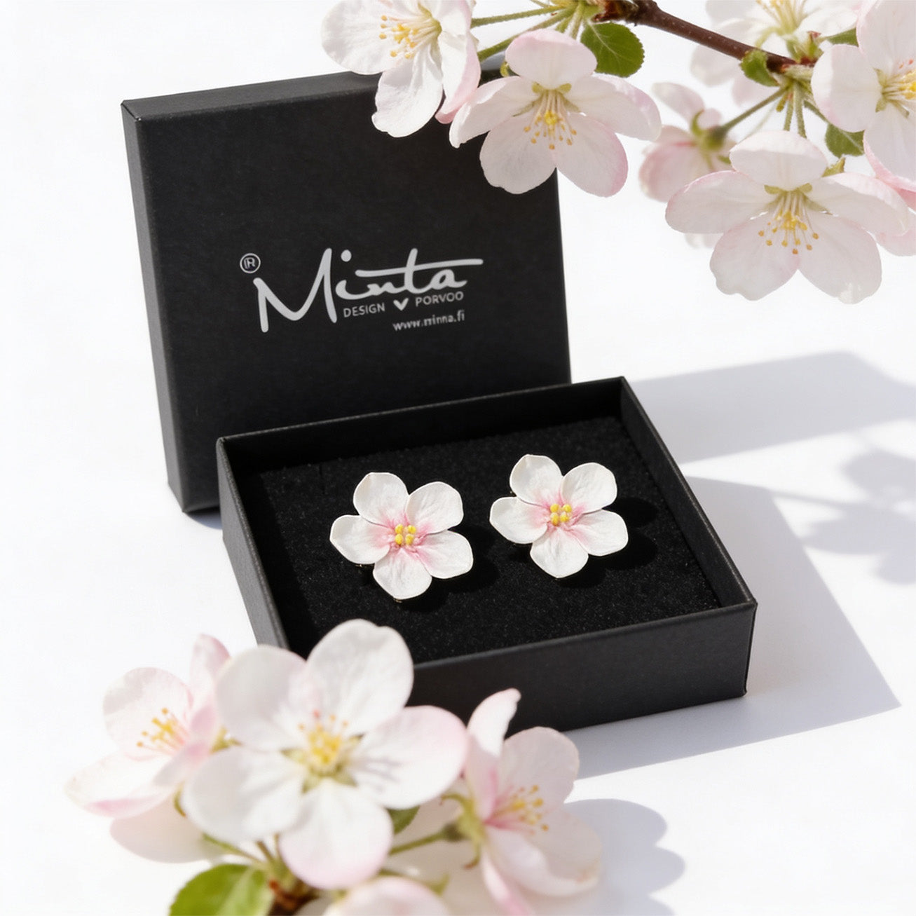 Apple blossom stud earrings by byMinta displayed in a jewelry box surrounded by soft blooming spring flowers in natural daylight.