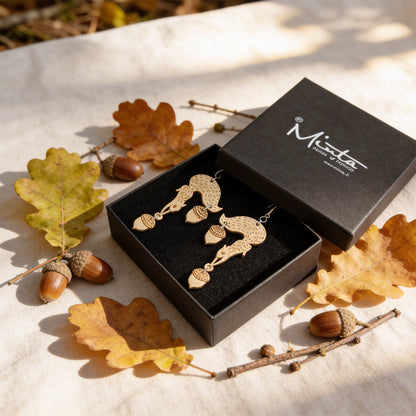 Handmade squirrel earrings displayed in a black jewelry box surrounded by oak leaves, acorns and small twigs. Lightweight Finnish birch plywood earrings styled in warm natural daylight with a soft Nordic autumn forest atmosphere.