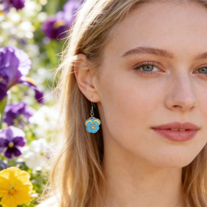 Close-up portrait of a Scandinavian woman wearing handmade sky blue pansy earrings in a blooming spring garden. Lightweight Finnish birch plywood floral earrings photographed in soft natural sunlight with a fresh Nordic atmosphere.