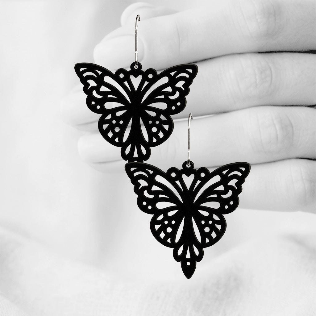 Black Papillon silicone earrings made in Finland, photographed against a black and white background of a hand.