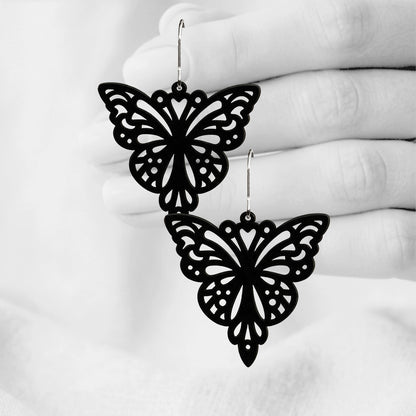 Black Papillon silicone earrings made in Finland, photographed against a black and white background of a hand.