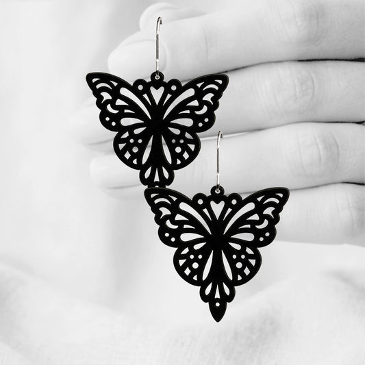 Black Papillon silicone earrings made in Finland, photographed against a black and white background of a hand.