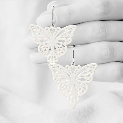 White Papillon silicone earrings made in Finland, photographed against a black and white background of a hand.
