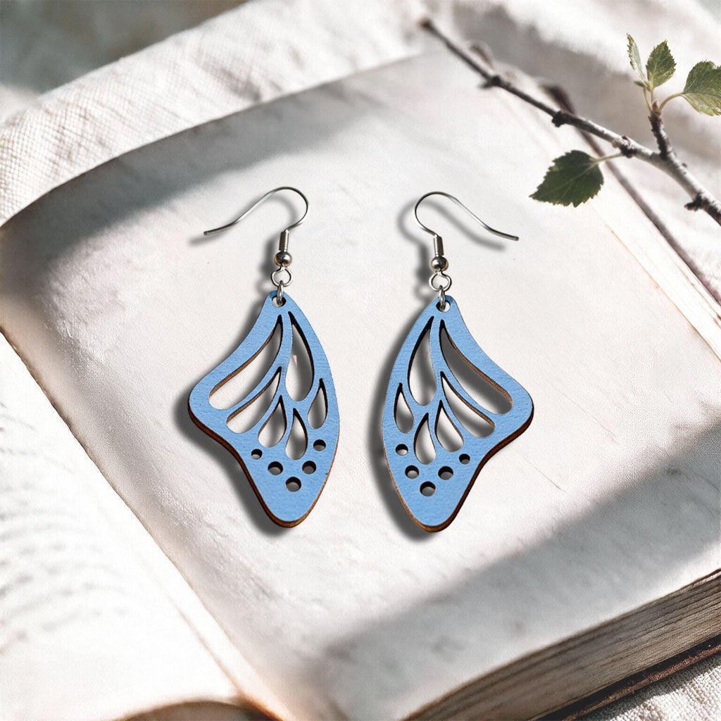 Light blue Butterfly Wing plywood earrings made in Finland, photographed on a vintage book in natural sunlight