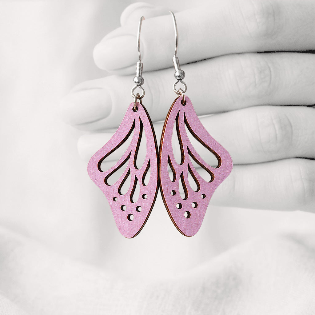 Mauve Perhosensiipi butterfly wing earrings made from Finnish birch plywood, photographed hanging from a hand against a softly blurred light background.