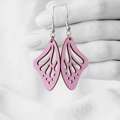 Mauve Perhosensiipi butterfly wing earrings made from Finnish birch plywood, photographed hanging from a hand against a softly blurred light background.