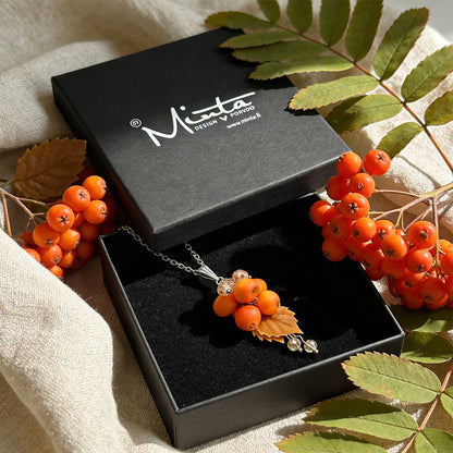 Rowan Berry Necklace presented in a gift box, surrounded by natural linen fabric, bright orange rowan berries, and green rowan leaves in soft natural light. Handmade necklace with hand-shaped berries and leaves, handmade in Finland by byMinta.