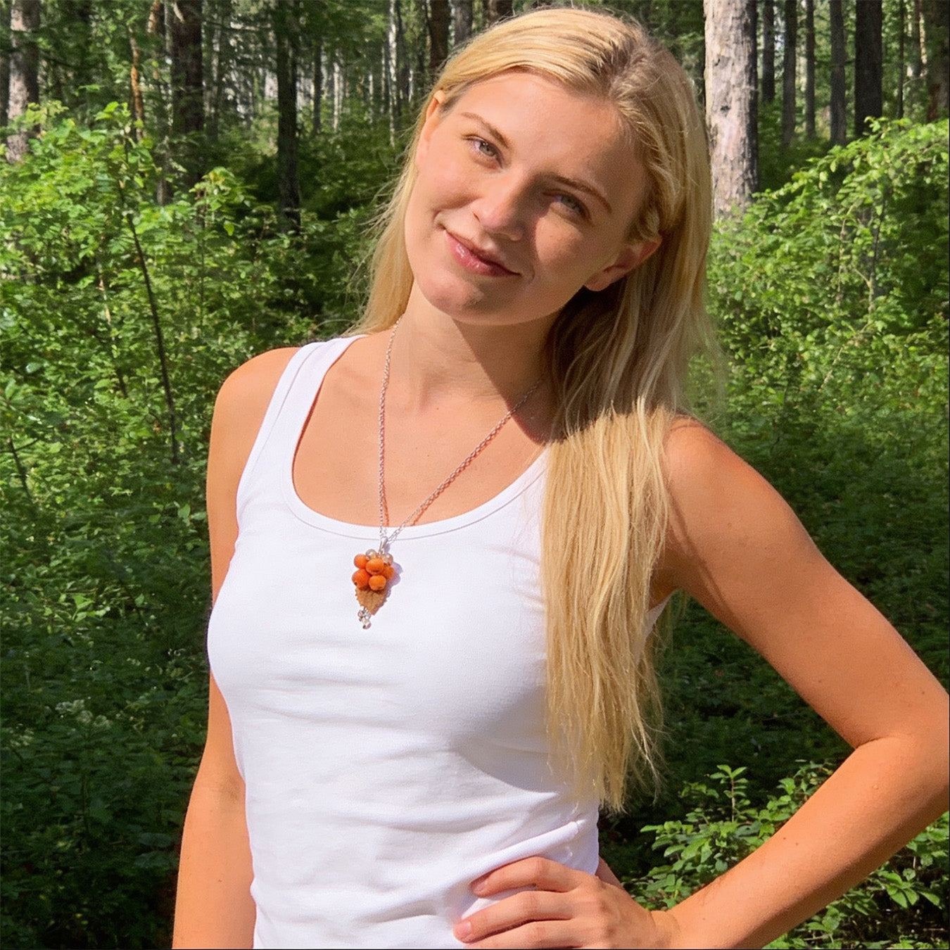 Blonde woman wearing the Rowan Berry Necklace in a sunlit Nordic forest. Handmade necklace with hand-shaped orange berries and leaves, photographed in natural summer light. Handmade in Finland by byMinta.