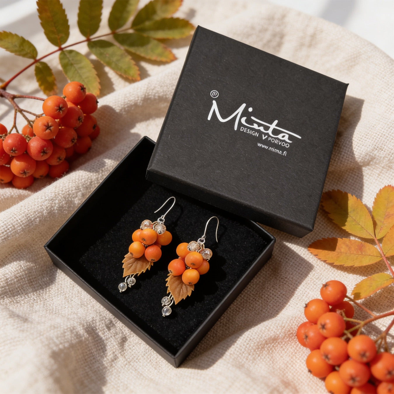 Rowan Berry Earrings presented in a gift box, surrounded by natural linen fabric, fresh rowan berry clusters, and autumn leaves. Handmade in Finland by byMinta.