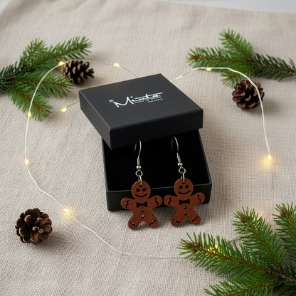 Gingerbread cookie earrings presented in a gift box with pine branches, pinecones, and warm fairy lights, creating a festive Christmas atmosphere. Handmade in Finland by byMinta.