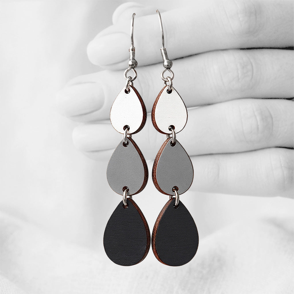 Black, grey and white Sadetta (Rain) plywood earrings made in Finland, featuring intricate laser-cut patterns and silver-toned hooks, photographed hanging from a hand against a softly blurred light linen background.
