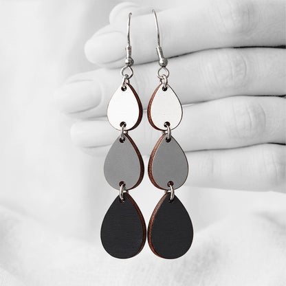 Black, grey and white Sadetta (Rain) plywood earrings made in Finland, featuring intricate laser-cut patterns and silver-toned hooks, photographed hanging from a hand against a softly blurred light linen background.