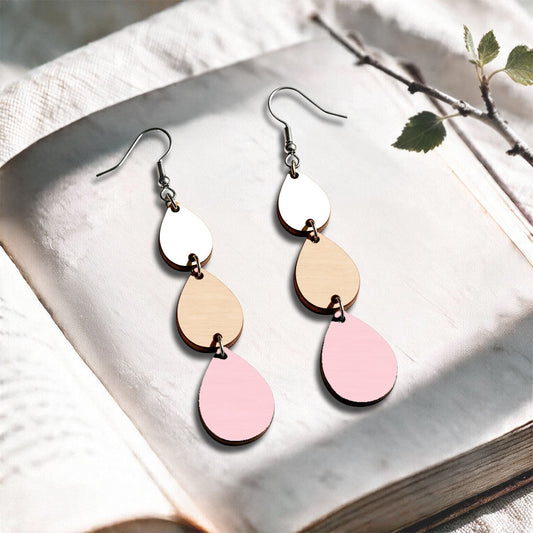 Pink, nude and white Sadetta plywood earrings made in Finland, photographed on a vintage book in natural sunlight