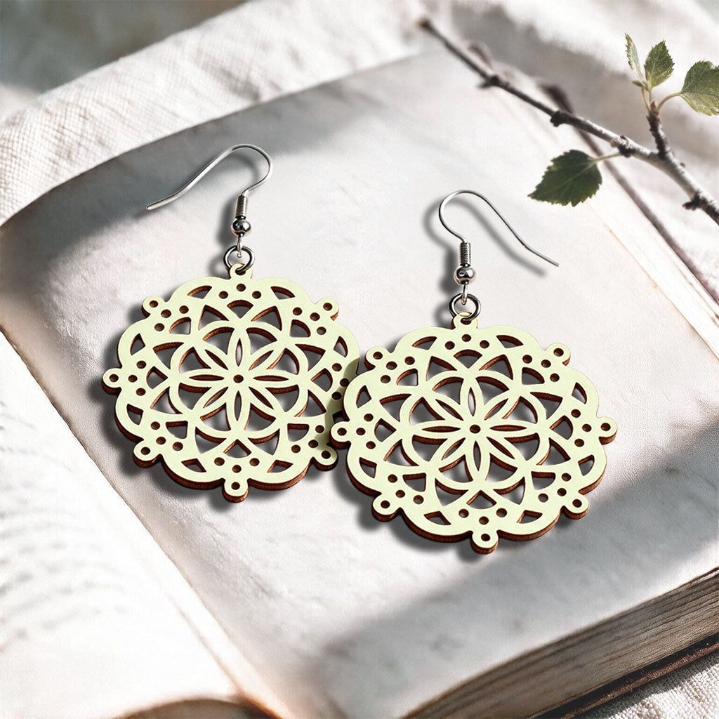 Vanilla Lace Mandala plywood earrings made in Finland, photographed on a vintage book in natural sunlight