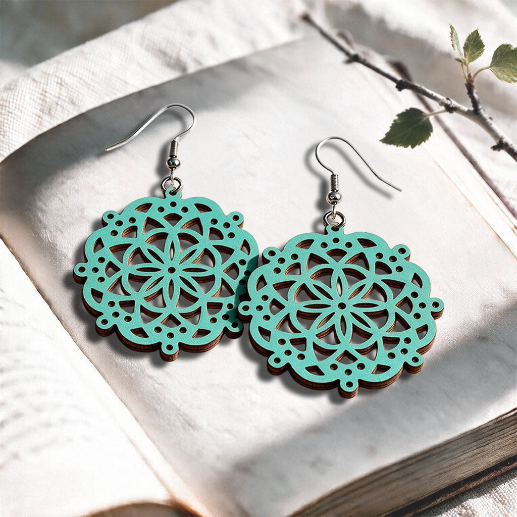 Turquoise Lace Mandala plywood earrings made in Finland, photographed on a vintage book in natural sunlight
